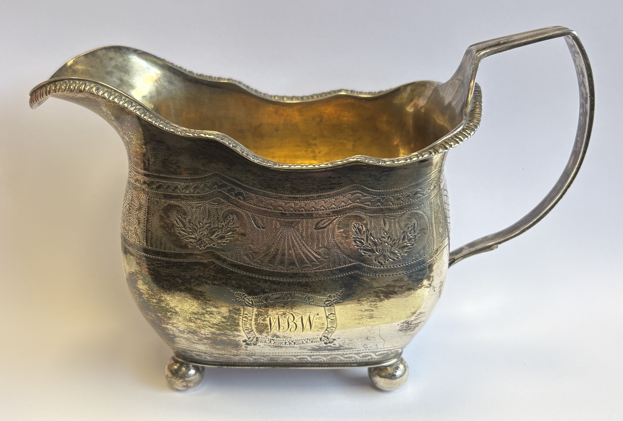 Victorian silver cream jug with engraved decoration on four ball feet