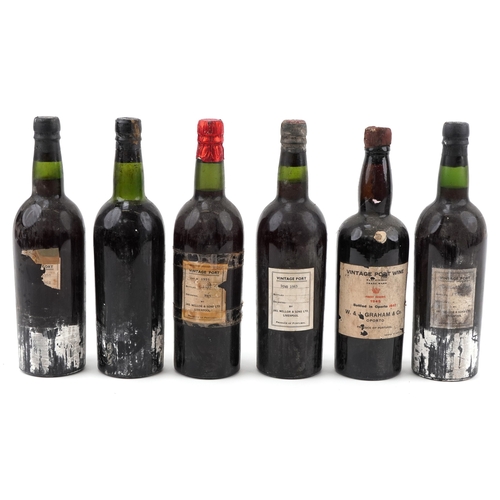 Six dusty vintage port bottles with mixed capsule colours, scuffed glass, replacement labels, and one prominently labelled W and J Graham 1945 bottle