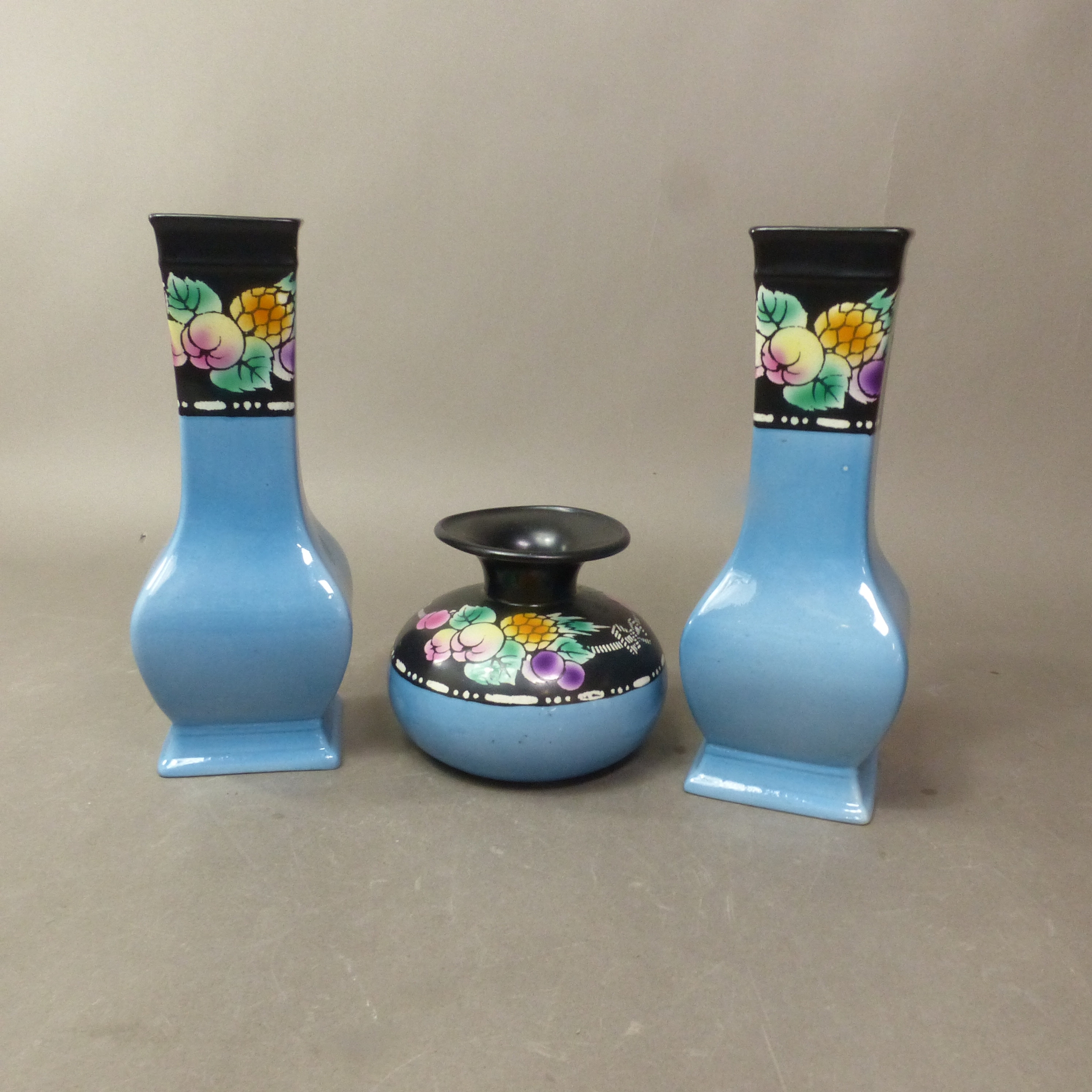 Two tall Shelley Art Deco vases and a squat companion vase in pale blue with black shoulders and brightly painted fruit decoration