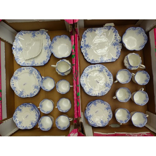 Shelley Dainty Blue tea service laid out across a table with stacked cups and saucers, cake plates, milk jugs, sugar bowls, and matching blue floral border decoration
