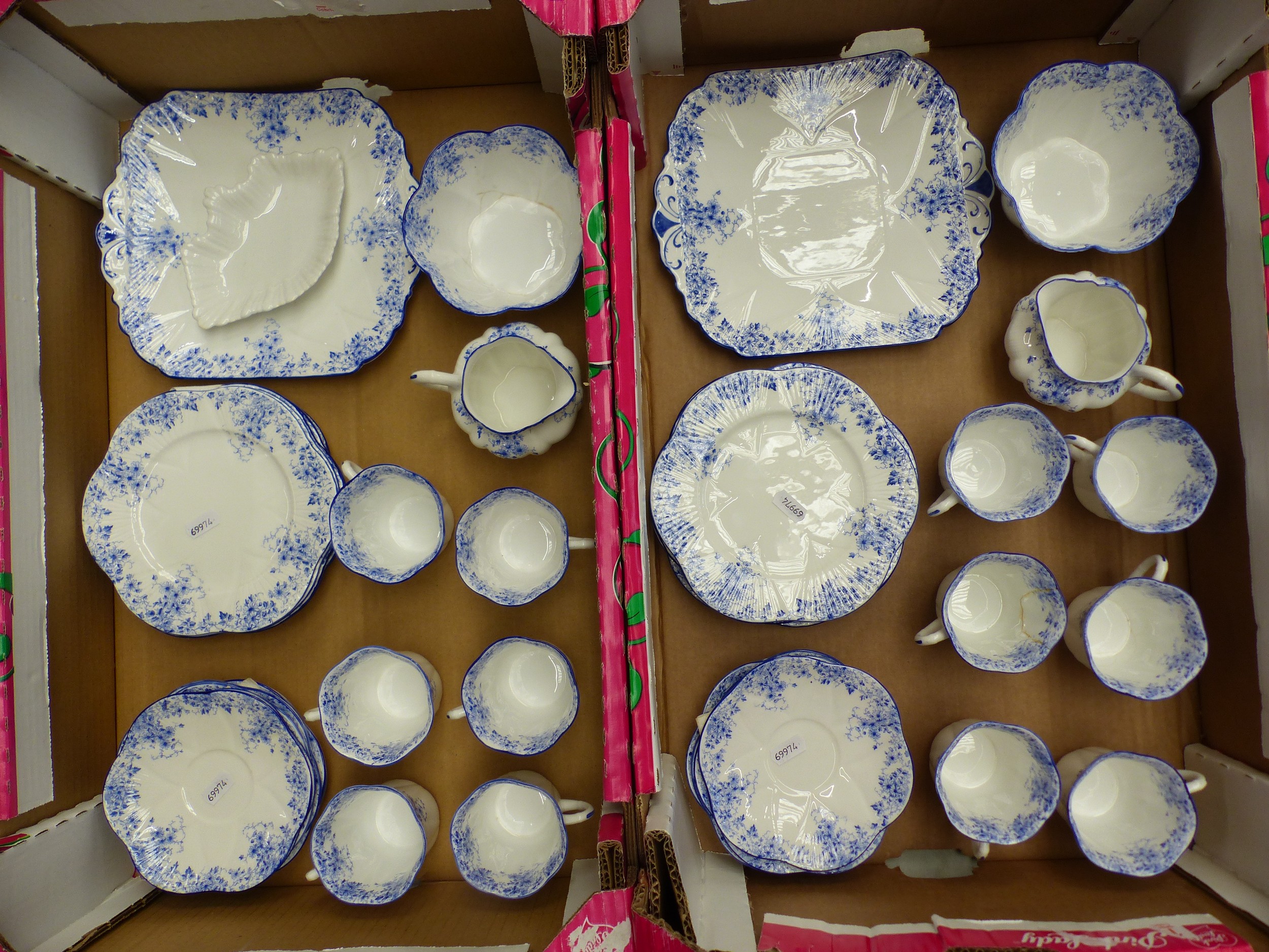 Shelley Dainty Blue tea service laid out across a table with stacked cups and saucers, cake plates, milk jugs, sugar bowls, and matching blue floral border decoration
