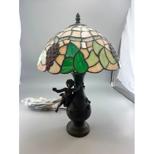 Tiffany-style table lamp with cream stained-glass shade, green leaf panels, dark red grape cabochons, and a dark cherub-mounted base